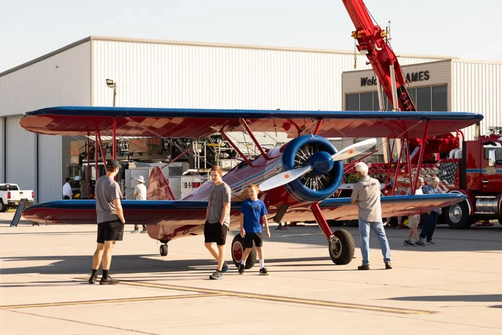 A family looking at a red propeller plane.