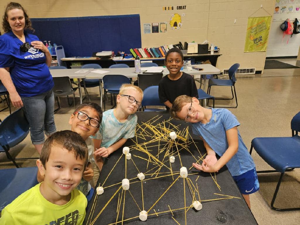 Kids posing with a project involving marshmallows and dry spaghetti noodles.