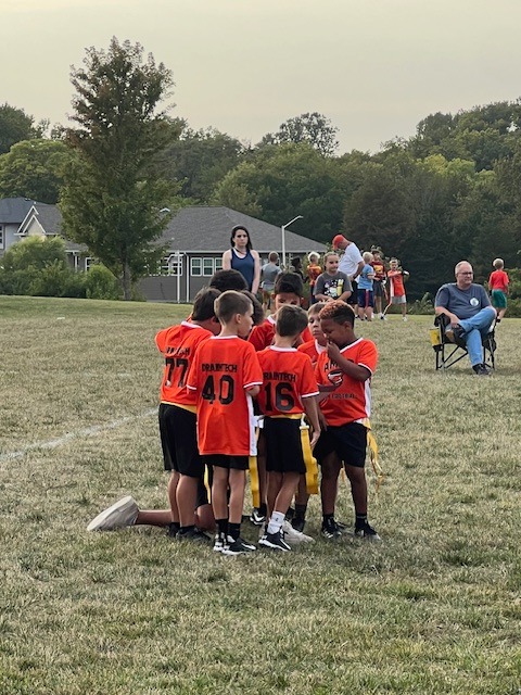 Kids in soccer jerseys on a soccer field huddled together.