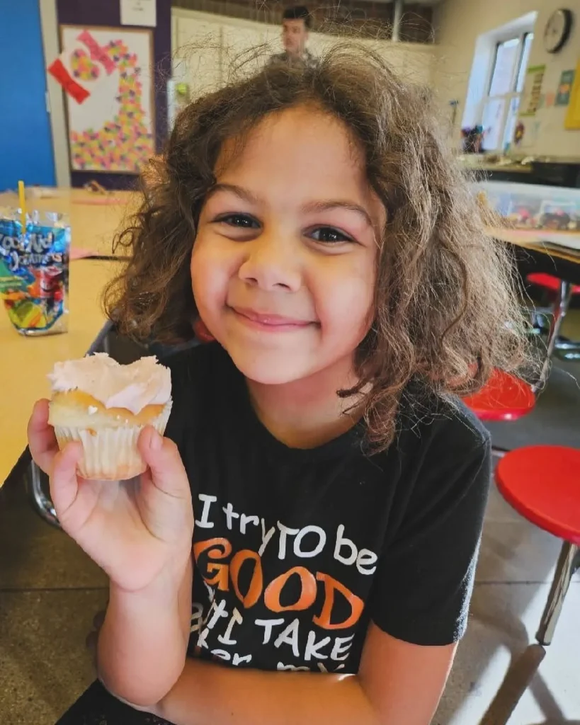 A girl posing with a valentines day cupcake.