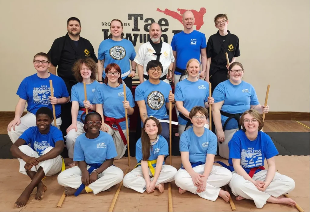 Kids in Taekwondo posing together for a picture in front of Brookings Taekwondo logo.