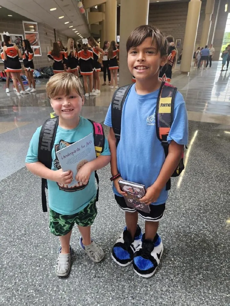 Two young boys holding books and wearing backpacks.