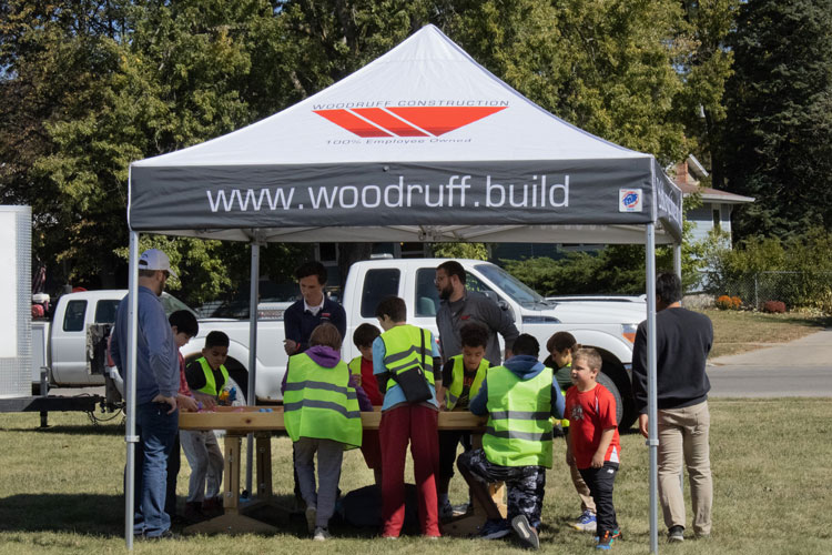 Kids wearing yellow safety vests participating in Construction day under a Woodruff Construction tent.